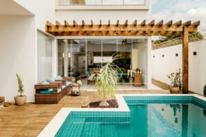 A photograph of the exterior of a home with a wooden pergola and swimming pool.