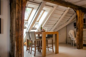 A photograph of a room with a table set in front of two skylights installed on a slanted ceiling.