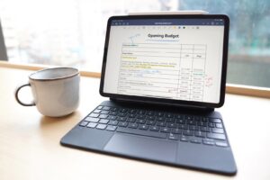 Photograph of an open latop with a budget document on the screen and a coffee cup beside the laptop.